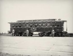 black and white image of Abraham Lincoln's funeral rail car with three soldiers standing alongisde it