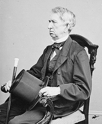 black and white image of William H. Seward seated in a chair and holding a top hat and a cane